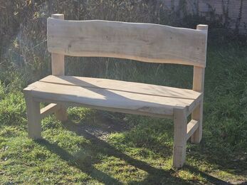 A handmade wooden bench with a backrest outdoors on grass