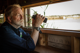 Photo - George McGavin in a bird hide with binoculars