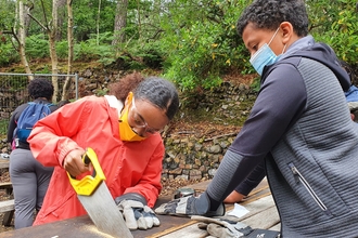 Photo showing two young people on an Explorers Visit, sawing a piece of wood on Brownsea Island