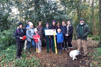 Photo showing work party at Bluebell Community Woodland standing around new information board 