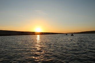 A view from the Fleet explorer boat with the sun low over Chesil bank