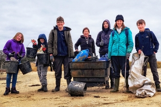A group of young people stand on a beach with rubbish they have collected