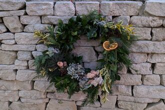 A festive wreath made using natural materials with a dry stone wall behind.