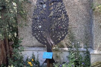 A metal tree sculpture with gold metal birds attached with commemorative messages outside in a garden