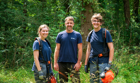 3 wardens stand in a woodland glade smiling with safety equipment