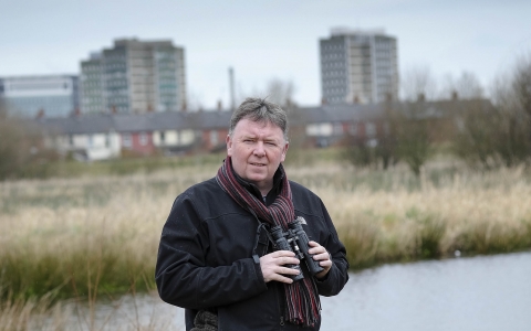 Aidan stands with his binoculars on a reserve