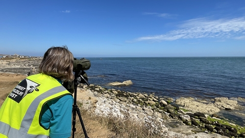 Someone at the waters edge using a scope to look out to sea