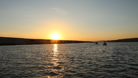 A view from the Fleet explorer boat with the sun low over Chesil bank 