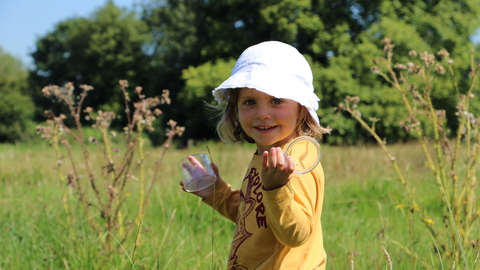 Girl in meadow with bug pot