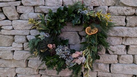 A festive wreath made using natural materials with a dry stone wall behind.