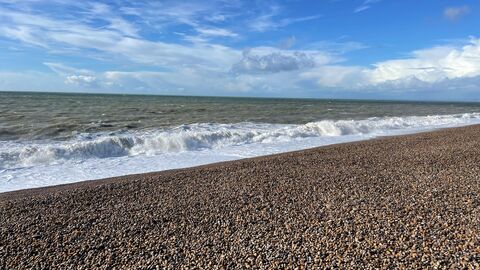 Waves crashing onto the shingle of Chesil Beach under blue skies
