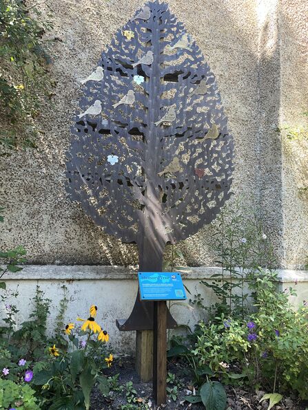 A metal sculpture of a tree with metal birds attached with commemorative messages etched in
