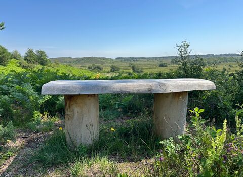 A handmade wooden bench, overlooking a green heath with a blue sky